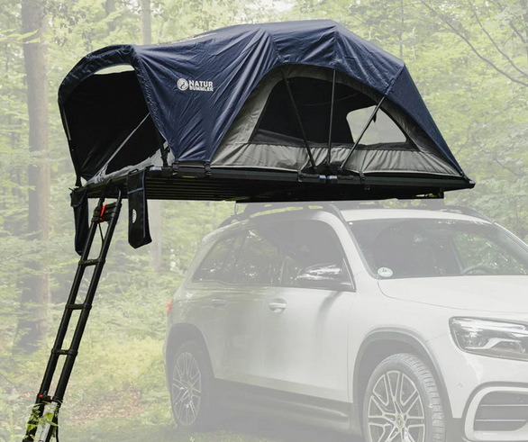 Ein dunkelblaues Dachzelt mit Leiter auf einem weißen Auto im grünen Wald